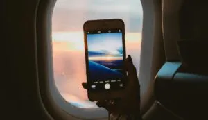 A person takes a photo of a sunset through an airplane window using a smartphone.